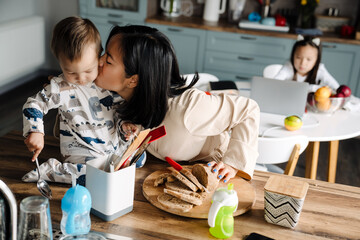 Wall Mural - Happy mother kissing her son while cutting bread