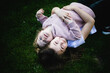 Dwie siostry przytulają się i leżą plecami na zielonej trawie