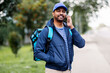 © Syda Productions - food shipping, profession and people concept - happy smiling indian delivery man with thermal insulated bag on city street calling on smartphone