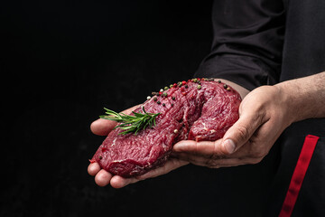 Wall Mural - male hands holding beef meat on a dark background, Whole piece of tenderloin with steaks and spices ready to cook, Long banner format