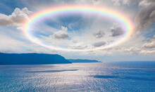 Scenic Sky Cloudscape With Big Bright Rainbow Above Sea, Blue Mountains In The Background
