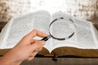 A magnifying glass in hand with open bible book.