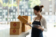 © Natee Meepian - Young business woman working online e-commerce shopping at her shop. Young woman seller prepare parcel box of product for deliver to customer. Online selling, sme, e-commerce.