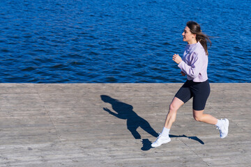 Athletic young woman running along the embankment