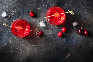 Poster - Cocktail cherry and a mocktail on a dark background, a vibrant red drink with ice, two glasses, an overhead shot with a place for text