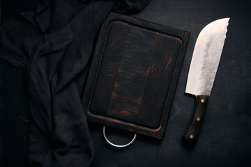 Wall Mural - rectangular empty wooden cutting board and kitchen knife on black table with gauze napkin, top view