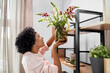 © Syda Productions - home improvement, decoration and people concept - happy smiling woman placing flowers to shelf