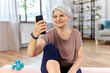 © Syda Productions - sport, fitness and healthy lifestyle concept - smiling senior woman with smartphone and wireless earphones exercising on mat at home