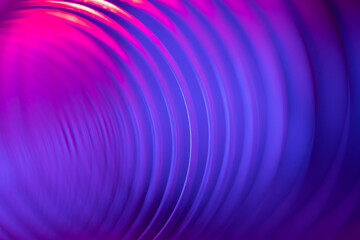 Closeup of coiled metal spring with sufficiently high strength and elastic properties in neon blue and pink light. Macro photo, selective soft focus. Abstract shot.