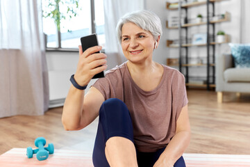 Poster - sport, fitness and healthy lifestyle concept - smiling senior woman with smartphone and wireless earphones exercising on mat at home