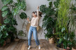 © DimaBerlin - Carefree young woman with long hair in wireless headphones listening to music with pleasure, enjoying the moment, relaxing dancing on wooden floor in cozy home garden with monstera and tropical plants