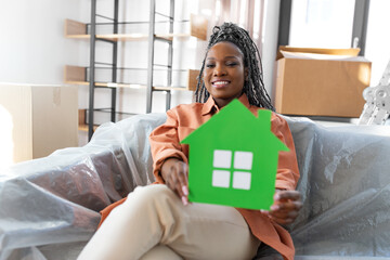 Poster - moving, people and real estate concept - happy smiling woman with green house and boxes sitting on sofa at new home