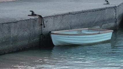 Wall Mural - A small wooden white boat stands at the pier in the port. Dark water. Cloudy day at the boathouse. Sea transport. Marina. The small port in a fishing village. Holidays on the coast. Water ripple.