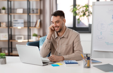 Sticker - distant education, school and remote job concept - happy smiling male teacher with laptop computer and earphones working at home office