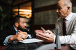 © Maskot - Senior male lawyer discussing over contract with colleague at desk in office