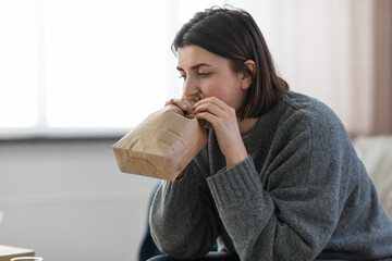 mental health and psychological problem concept - woman having panic attack breathing to bag at home