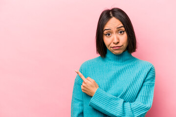 Wall Mural - Young hispanic woman isolated on pink background smiling and pointing aside, showing something at blank space.