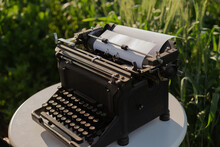 The End Inscription On Blank Paper Sheet Loaded Into A Retro Typewriter. Dream Writer's Workplace In Green Wheat Field. Inspiration, Creative Freedom And Remote Work Concept