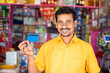 Smiling kirana or grocery merchant showing credit card by looking at camera at grocery shop - concept of credit card payment, shopping and small business.