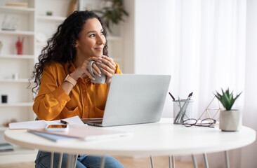 Poster - Dreamy Businesswoman Using Laptop And Holding Coffee Cup Indoors