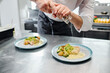 © AnnaStills - Close-up of chef adding spices from shaker on ready dishes on table before serving