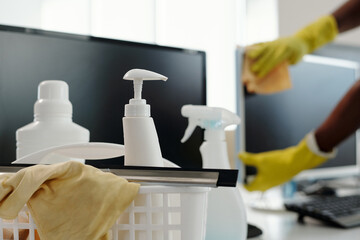 Poster - Group of detergents in white plastic bottles with dispensers and duster in basket against computer screen and gloved hands of man