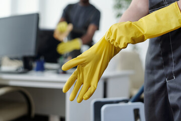 Poster - Hands of female worker of contemporary cleaning company putting on yellow protective rubber gloves before mopping floor of office