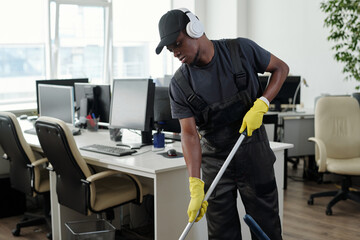 Poster - Young male staff of cleaning service company in headphones washing floor in large openspace office and listening to music