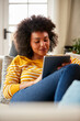 Woman Relaxing On Sofa At Home Using Digital Tablet To Stream Movie Or Shop Online