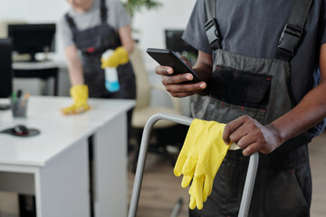 Aufkleber - Hands of young African American male cleaner of modern cleaning service company choosing music in smartphone during work