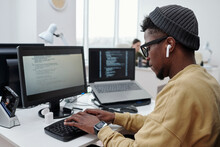 Side View Of Young Male Programmer Or It Developer In Casualwear Listening To Music In Earphones While Working In Office