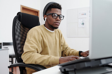 Poster - Young contemporary serious male it programmer in yellow sweatshirt looking at computer screen while decoding data in office