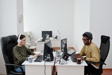 Poster - Side view of two young intercultural programmers working in front of computers while decoding data or developing new software