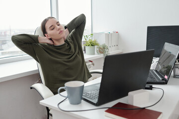 Poster - Young relaxed female programmer doing exercise for neck and arms while sitting by her workplace and looking at laptop screen
