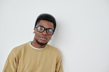 Poster - Young confident African American man in eyeglasses, beanie hat and sweatshirt standing by white wall in front of camera