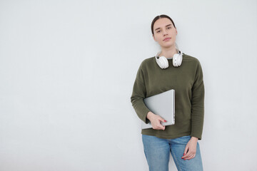 Poster - Young serious female student in blue jeans and dark green pullover looking at camera against white wall with copyspace