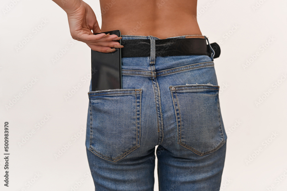 Buttocks of a girl in jeans close-up. The hand holds the phone sticking ...
