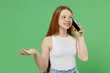 © ViDi Studio - Little redhead kid girl 12-13 years old wearing white tank shirt talk speak on mobile cell phone conducting pleasant conversation isolated on plain green background studio Childhood lifestyle concept.