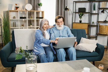 Wall Mural - Happy senior couple, happy husband overjoyed wife looking at laptop screen feel excited received fantastic news. Concept of online lottery win great commercial offer retirement and free time.