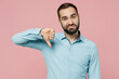 © ViDi Studio - Young dissatisfied displeased sad caucasian man 20s wear classic blue shirt showing thumb down dislike gesture isolated on plain pastel light pink background studio portrait. People lifestyle concept.