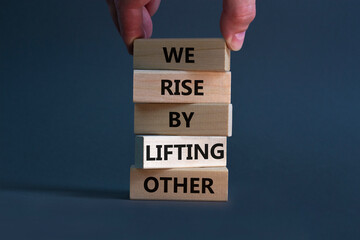 We rise by lifting other symbol. Concept words We rise by lifting other on wooden blocks. Businessman hand. Beautiful grey background. Business we rise by lifting other concept. Copy space.