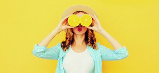 Poster - Summer portrait of cheerful young woman covering her eyes with slices of orange fruits and looking for something wearing straw hat on yellow background