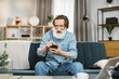 © sofiko14 - People home and using gadgets. Confident stylish man with grey beard smiling happily sitting on the couch at cozy living room indoors and using smartphone for typing message or serfing social networks