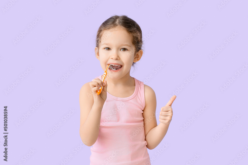 Adorable little girl brushing teeth on lilac background