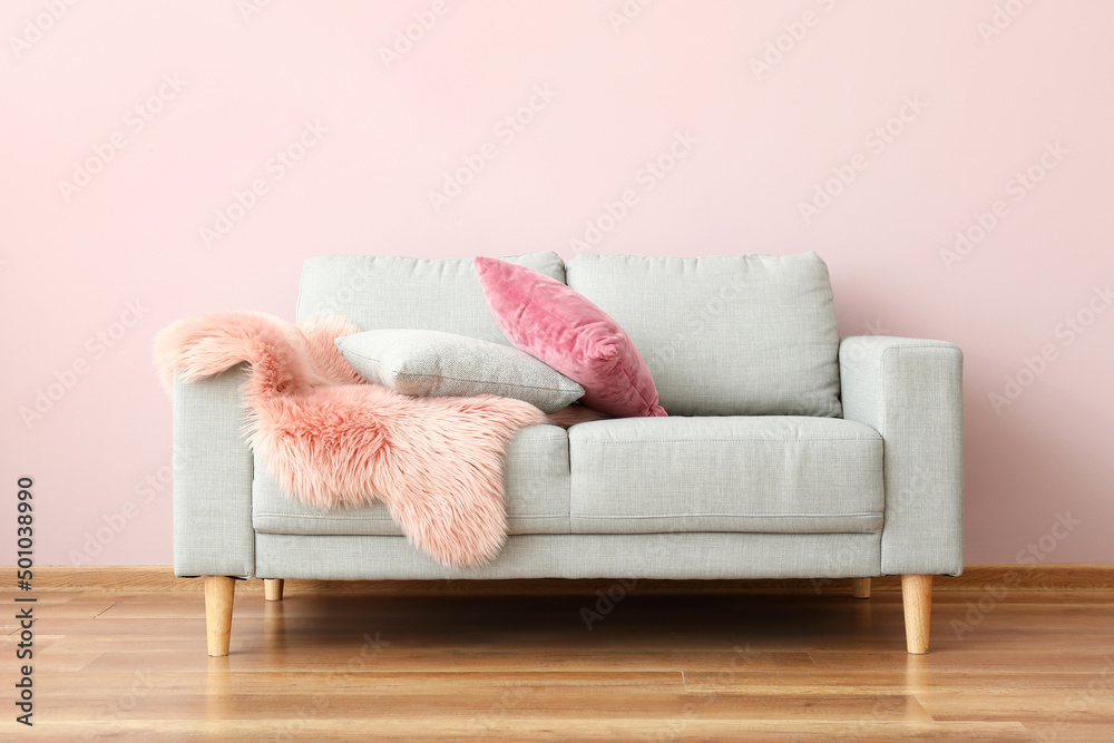 Modern sofa with pillows and plaid near color wall in room