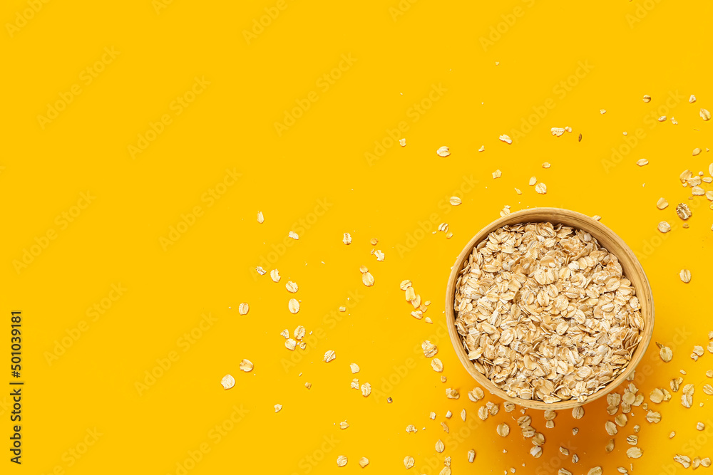 Bowl with raw oatmeal flakes on orange background
