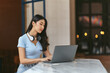 © PaeGAG - Asian young female student sitting at the table, using headphones when studying.