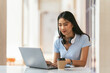 © PaeGAG - Asian young female student sitting at the table, using headphones when studying.