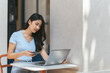 © PaeGAG - Portrait of beautiful Asian woman sitting outdoors at coffee shop restaurant during summer, using smart wireless technology computer laptop and smartphone, relaxing coffee break at cafe restaurant.