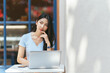 © PaeGAG - Portrait of beautiful Asian woman sitting outdoors at coffee shop restaurant during summer, using smart wireless technology computer laptop and smartphone, relaxing coffee break at cafe restaurant.